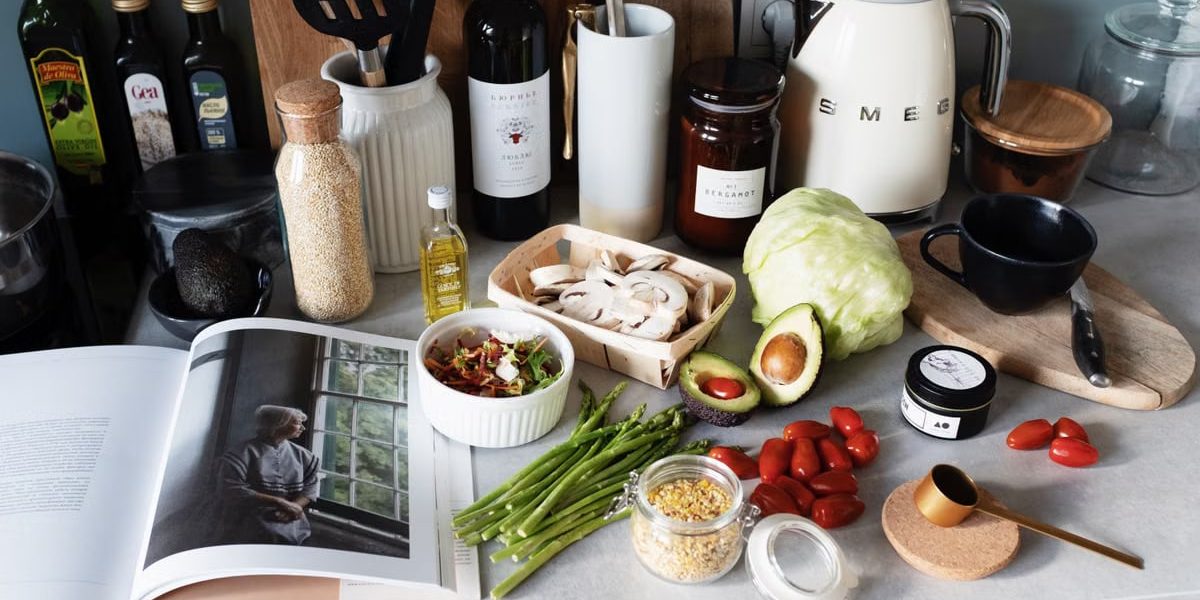 Various colorful healthy food and vegetables locating on countertop next to many different utensils and white kettle during cooking in stylish kitchen